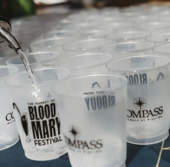 Frosted plastic cups with Blood Mary Festival and Compass Builders logos being filled with water