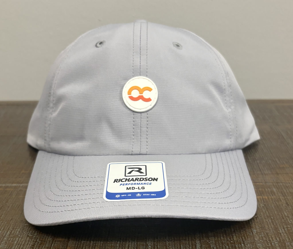 Light grey Richardson performance cap with a circular rubber patch featuring interlocking orange and coral C shapes