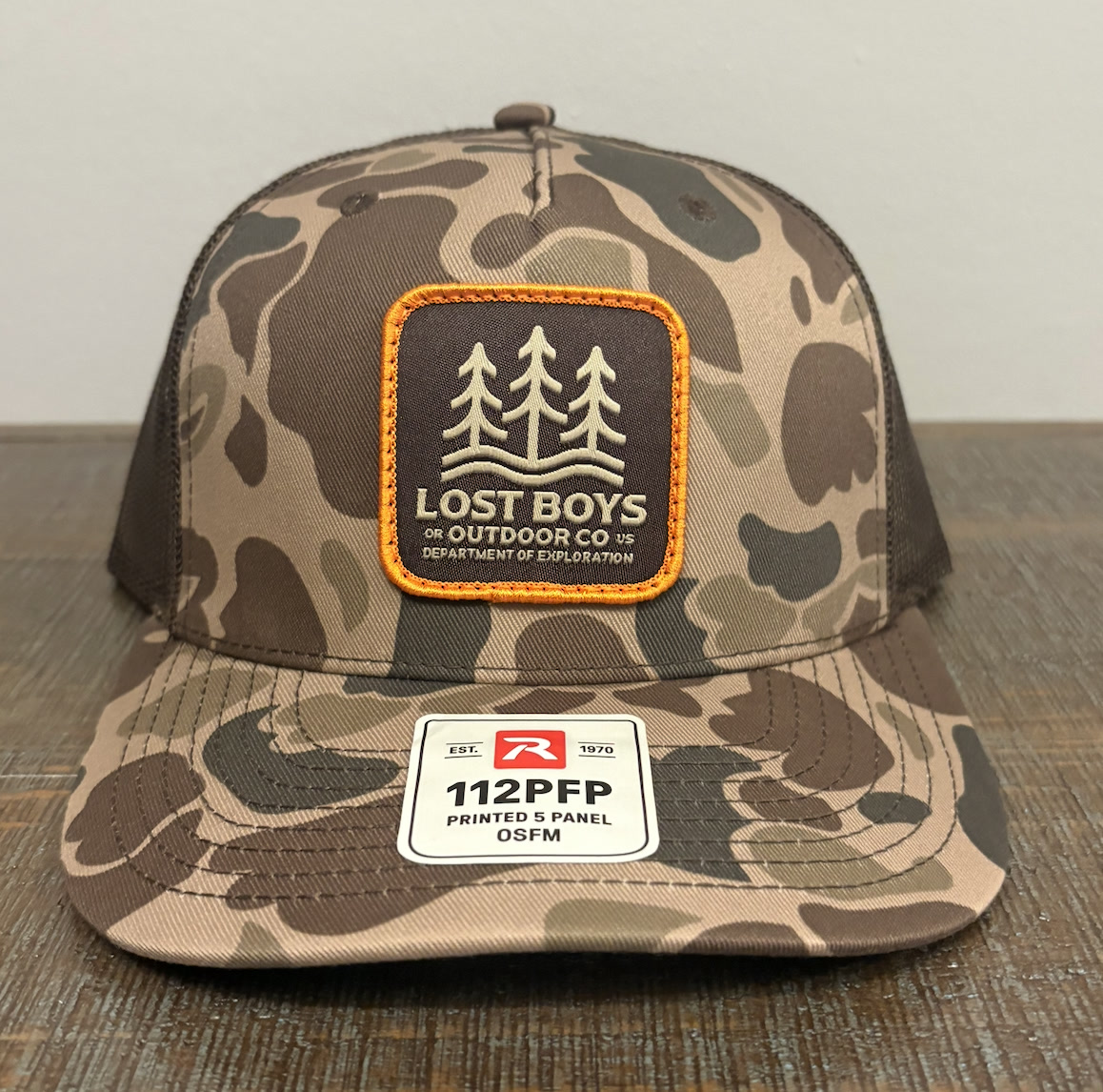 Camo trucker hat with a custom fabric patch featuring three pine trees and the Lost Boys Outdoor Co. logo