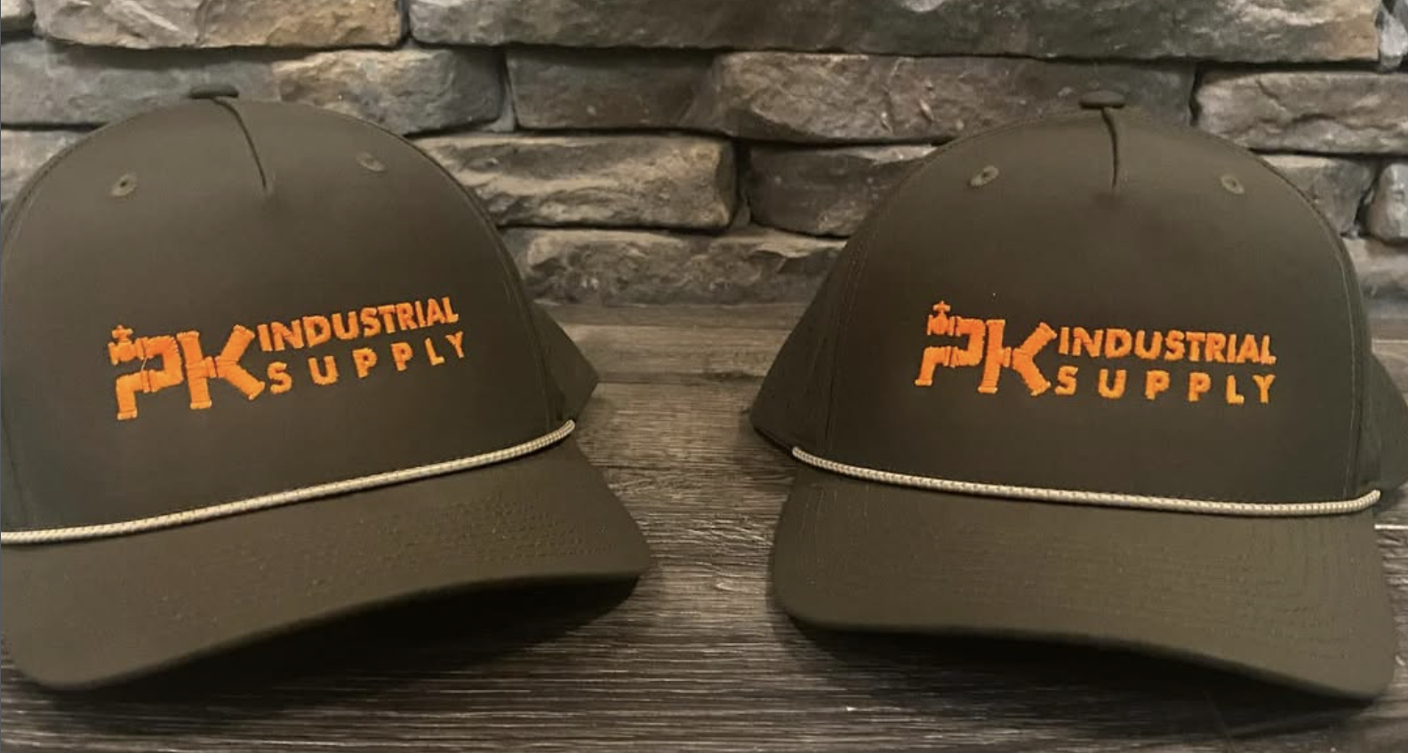 Two olive green caps with orange AK Industrial Supply embroidery